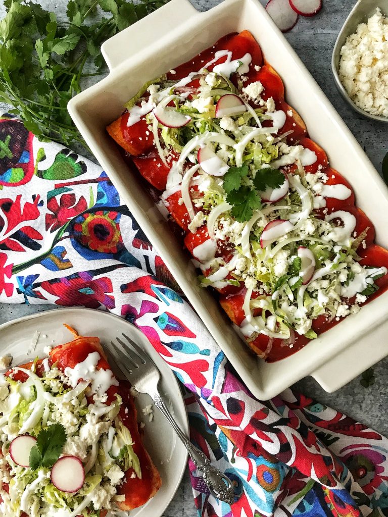 Pan of red enchiladas and plate with enchiladas and fork.