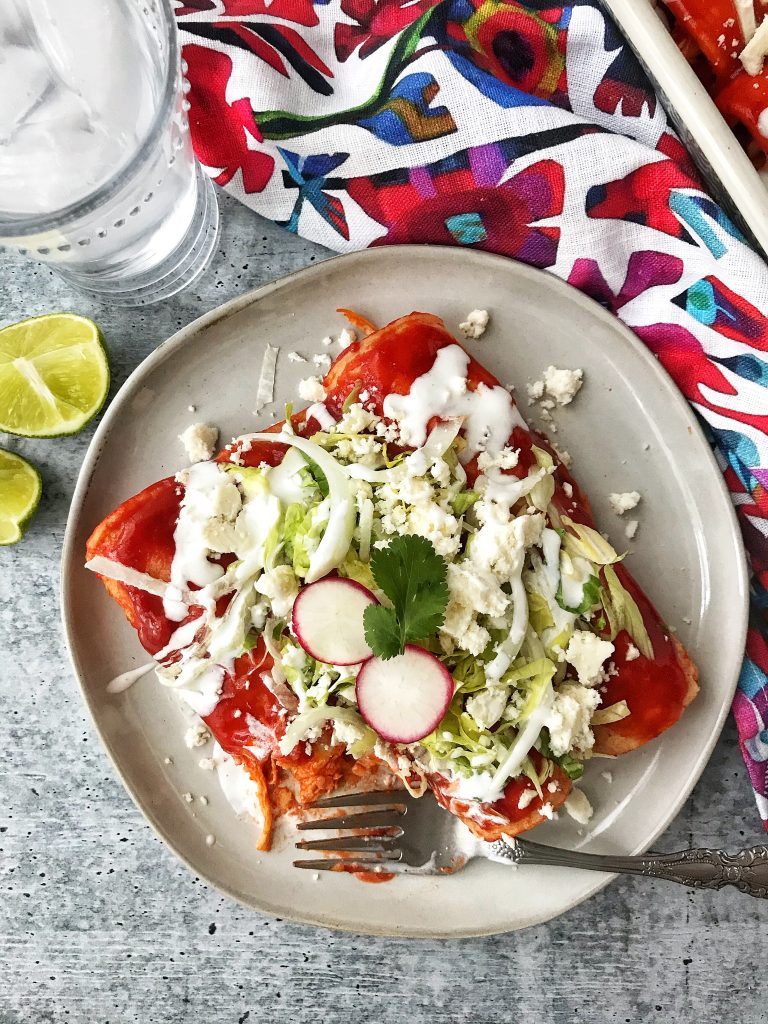 Plate with red enchiladas with fork. Drink and limes on the side.