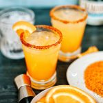 Orange and mango margaritas with orange wedge and Tajin rim