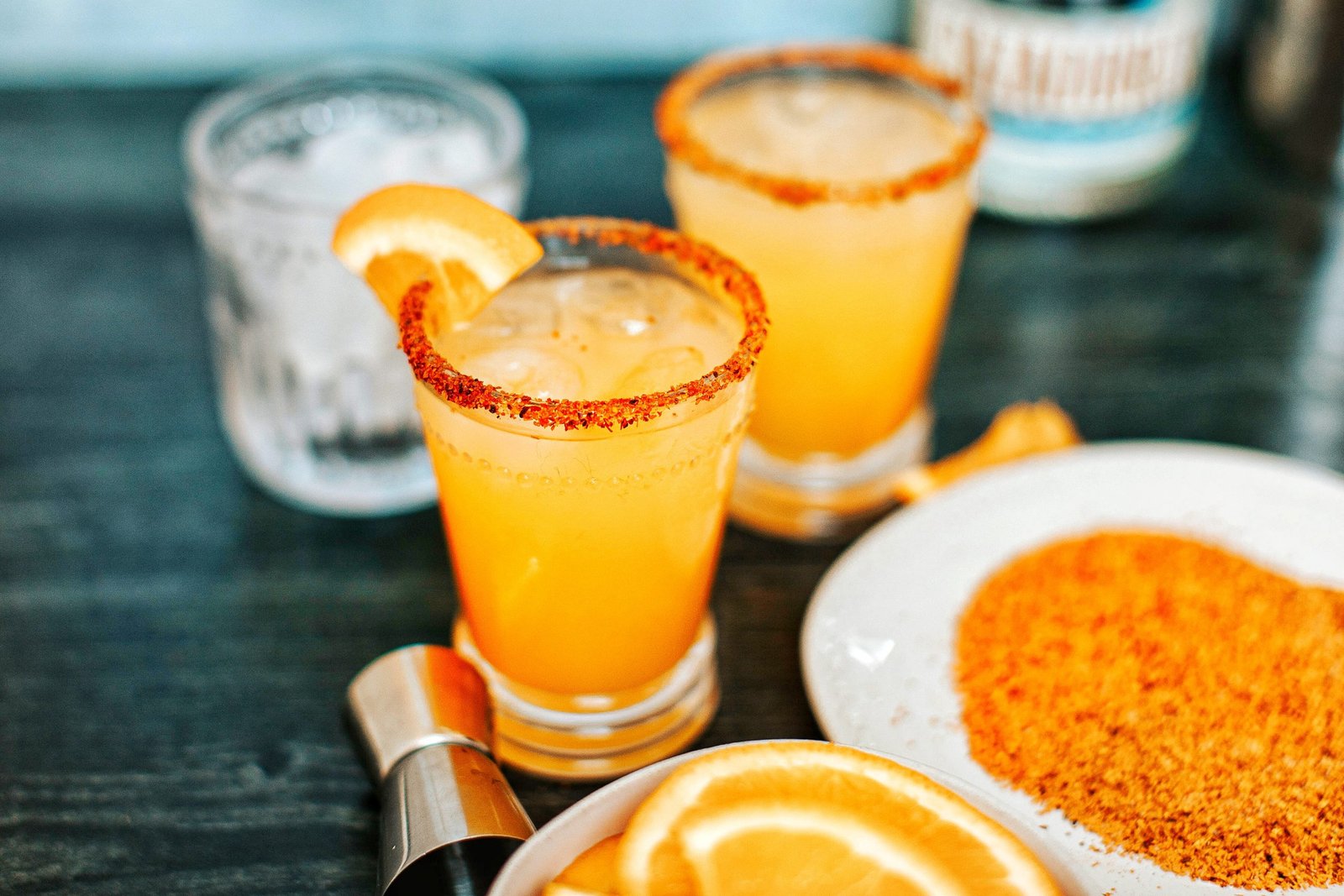 Orange mango margarita in glass with Tajin rim. Orange slices in bowl, Tajin on plate.