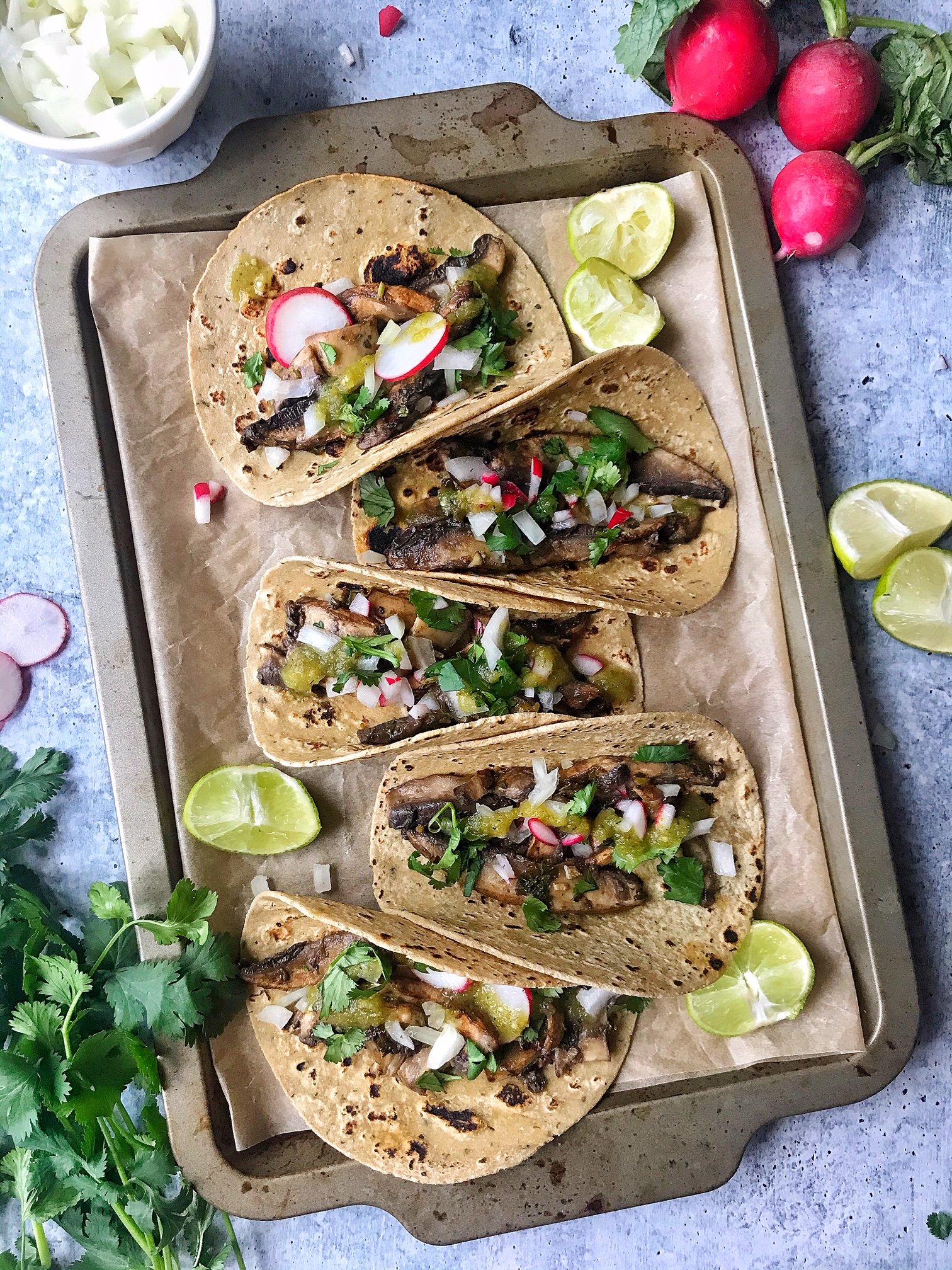 Mushroom Asada Tacos with onions, cilantro, salsa, and radishes. Tacos folded on a baking sheet.