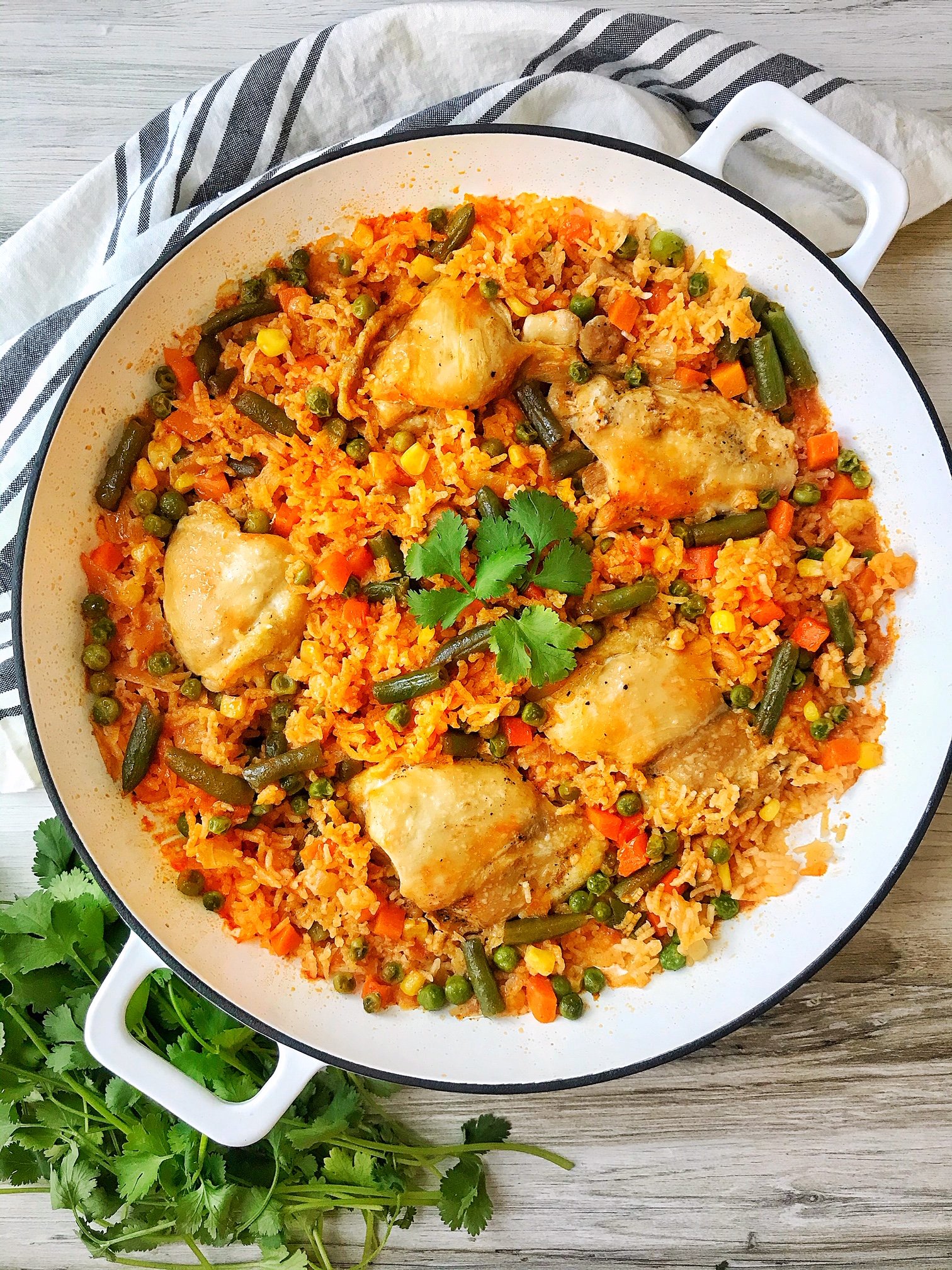 Large pan of arroz con pollo. Chicken thighs and rice with vegetables in a large white pan. Cilantro on the side.