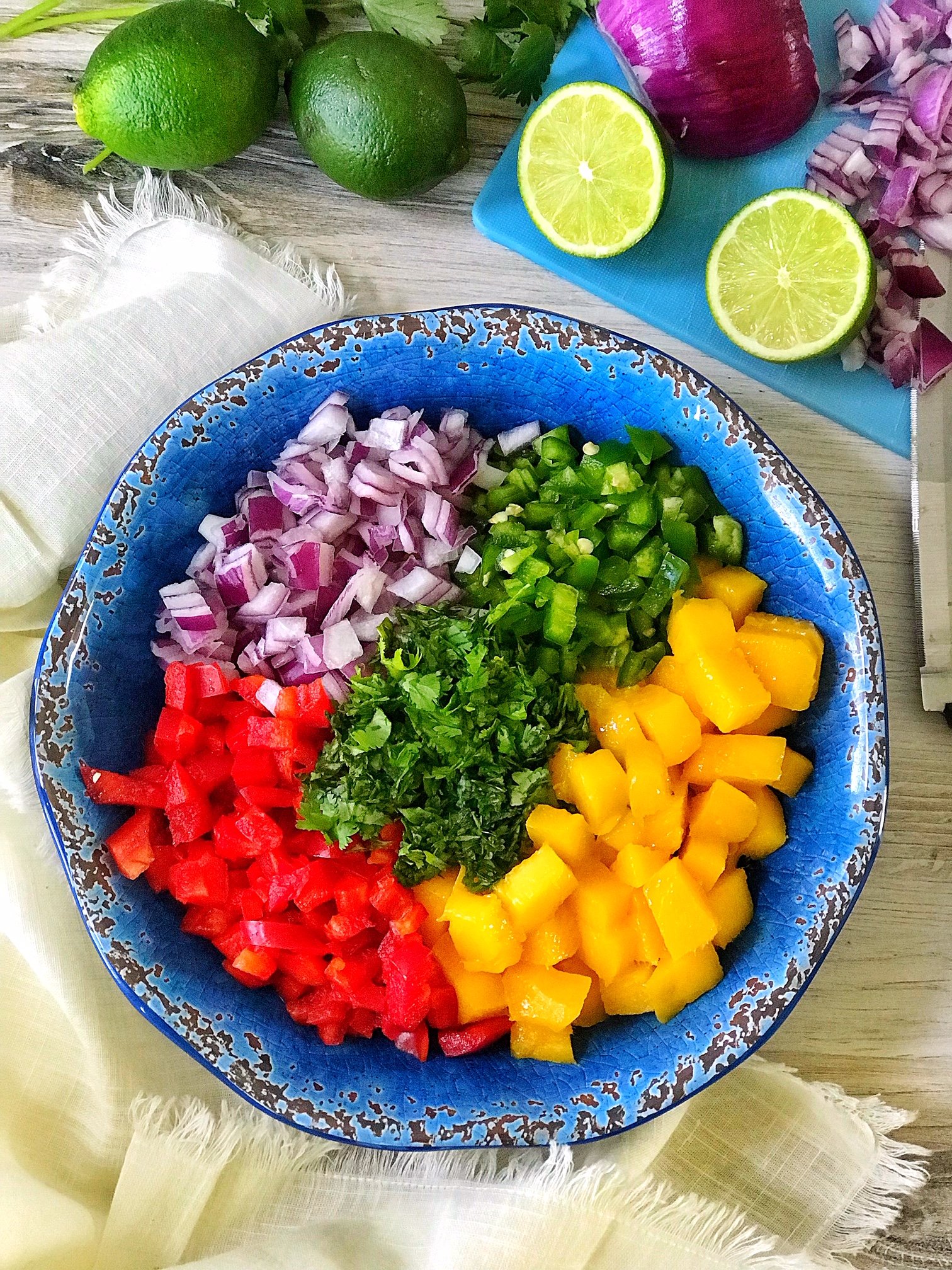 Mango salsa ingredients in blue bowl with chopped mango, red bell pepper, cilantro, and jalapeno.