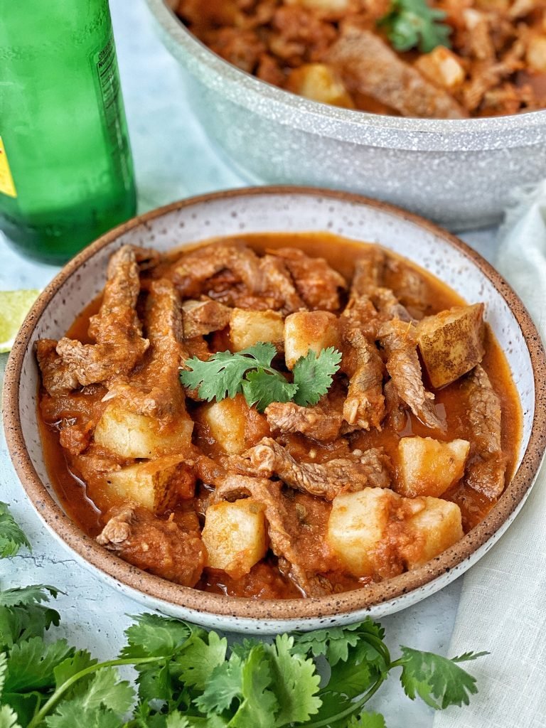 Bistec con papas (mexican steak and potatoes) in a white bowl with cilantro garnish.