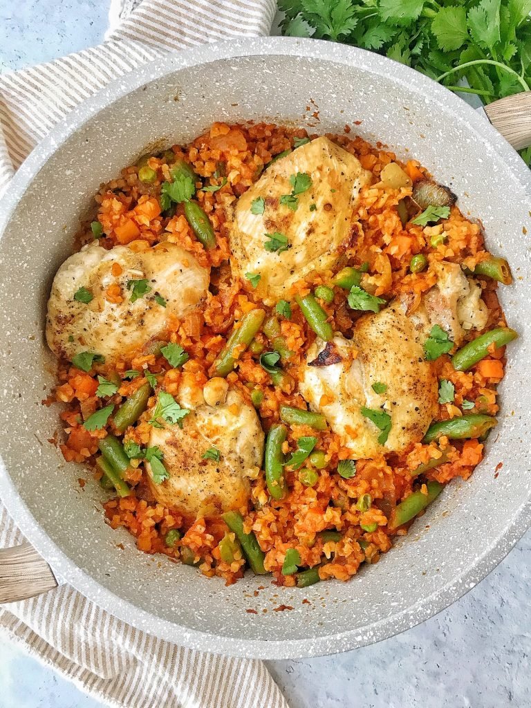 Pan with cauliflower rice and vegetables in tomato sauce with chicken thighs on top.