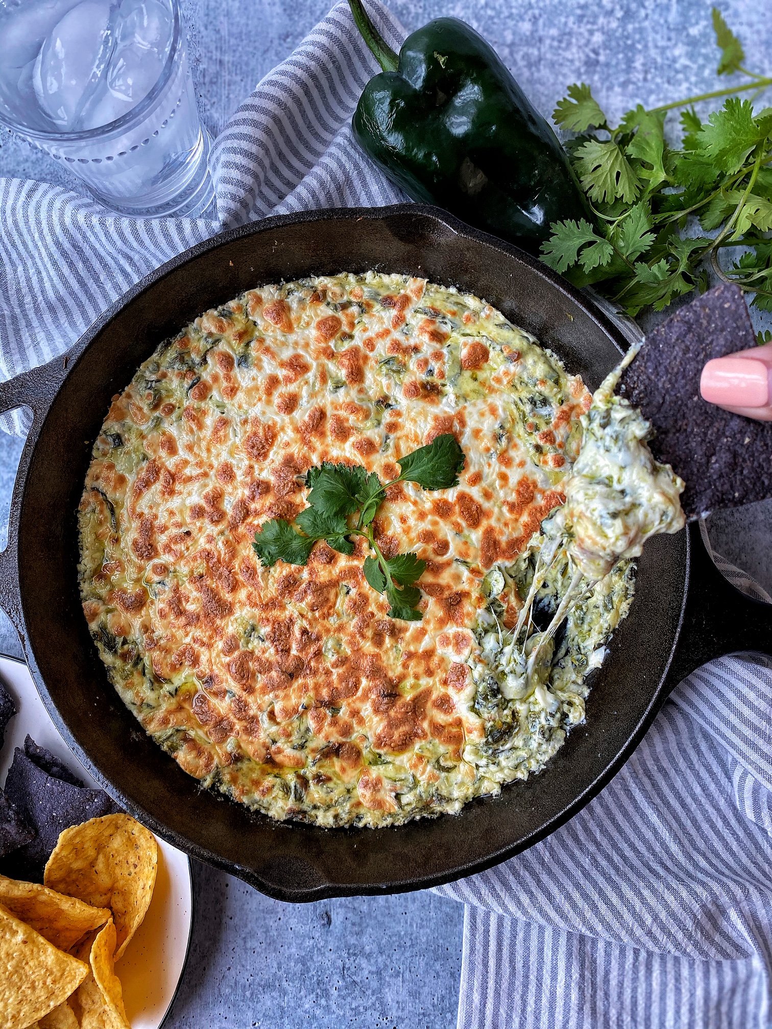 Cast iron with spinach poblano dip with chip dipped into dip. Poblano pepper on the side, cilantro garnish
