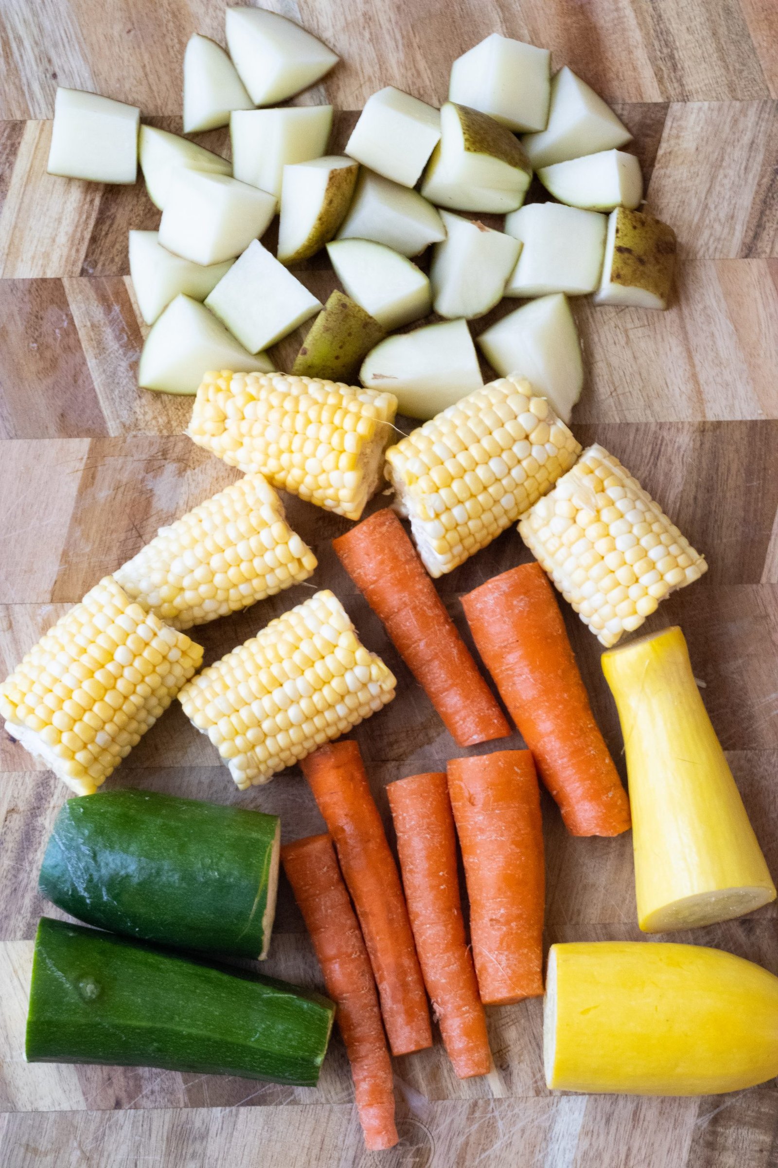 Cutting board with chopped potatoes, zucchini, and squash, and corn