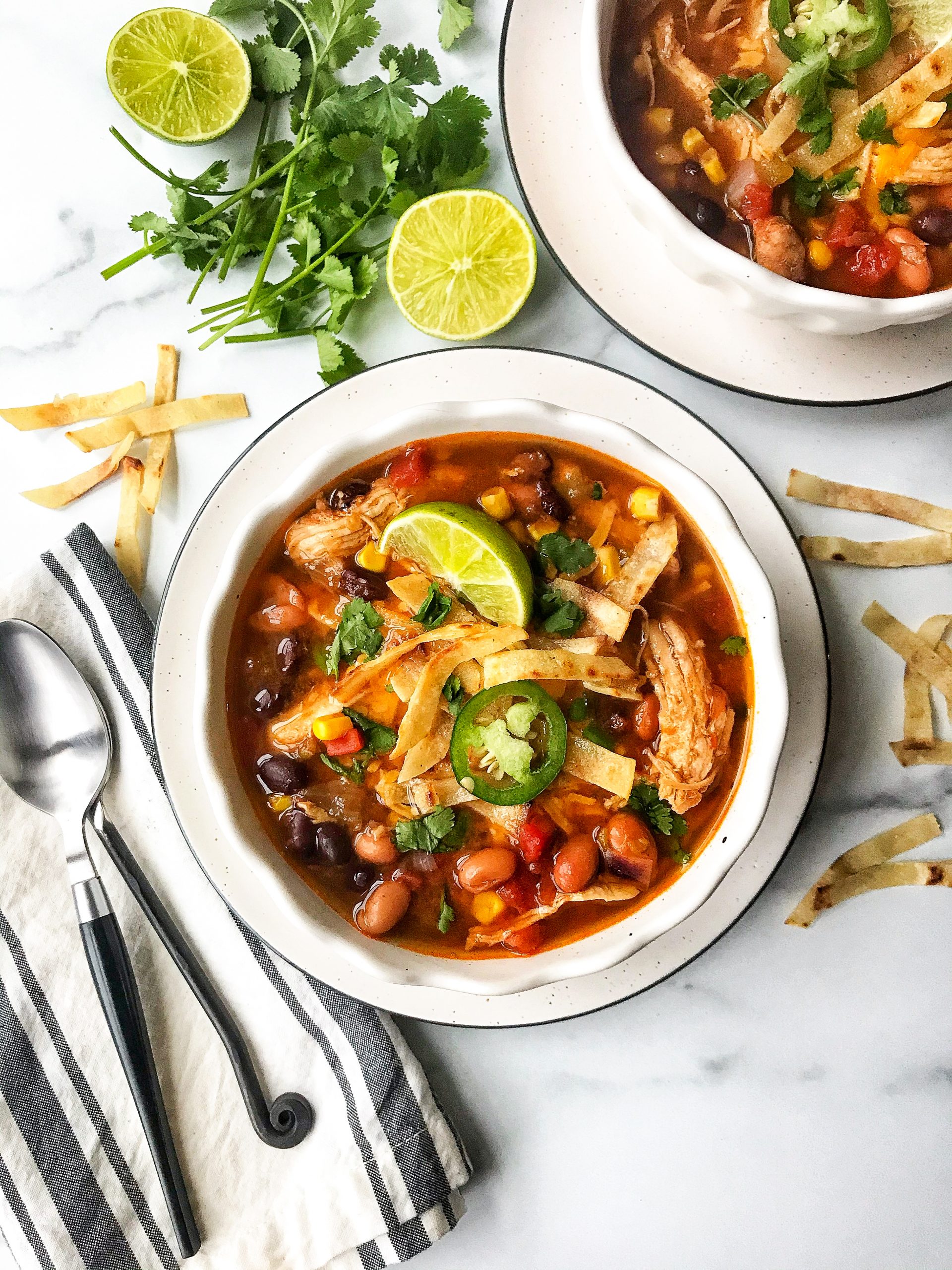 Two bowls of southwest chicken enchilada soup. Garnished with lime, tortilla chips, and jalapenos