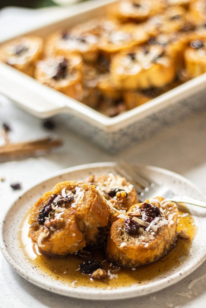 Capirotada, Mexican bread pudding, on a white plate. Topped with raisins, coconut flakes, and pecans.