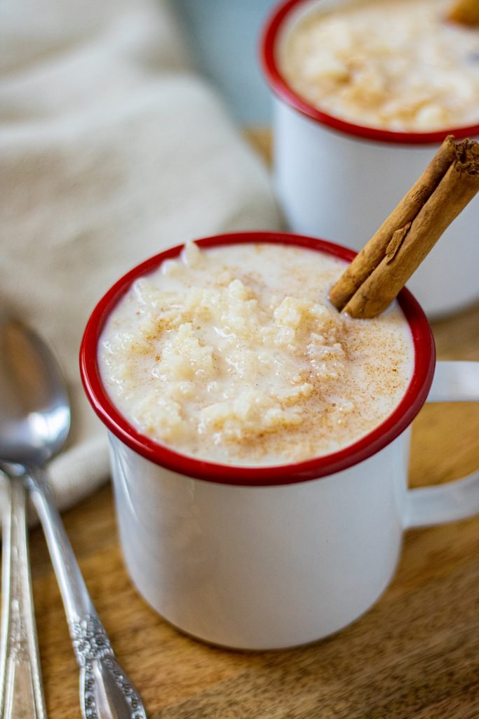 White mugs with red rims filled with arroz con leche. Garnished with a cinnamon stick.