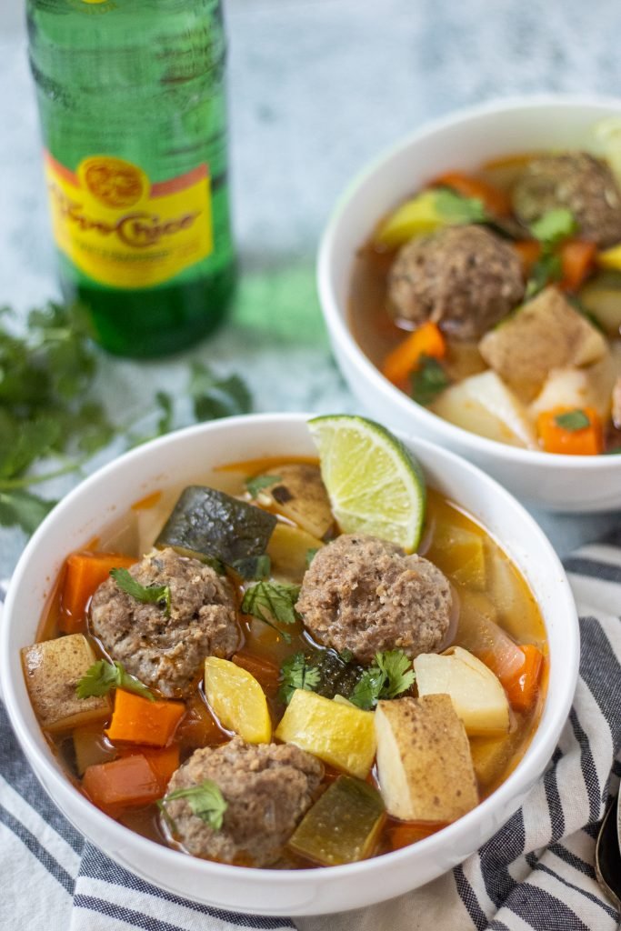 White bowl filled with albondigas, or meatballs, vegetables, and lime wedge garnish.