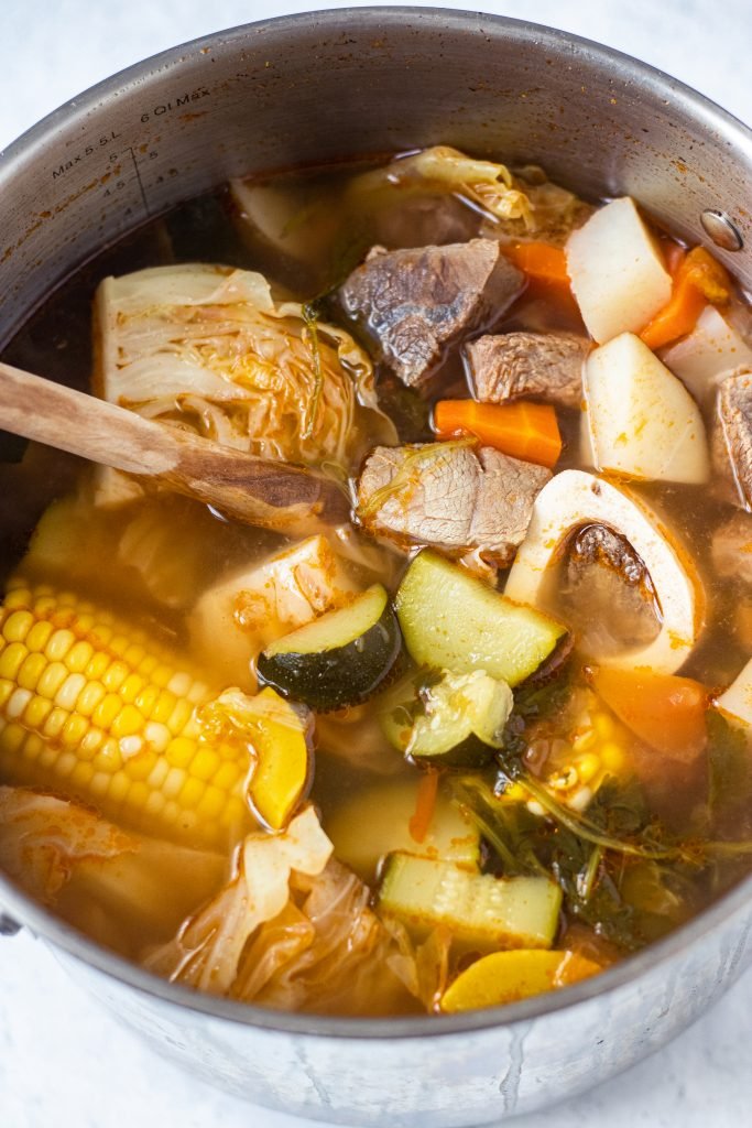 Large pot with caldo de res with corn, zucchini, carrots, cabbage, and beef.