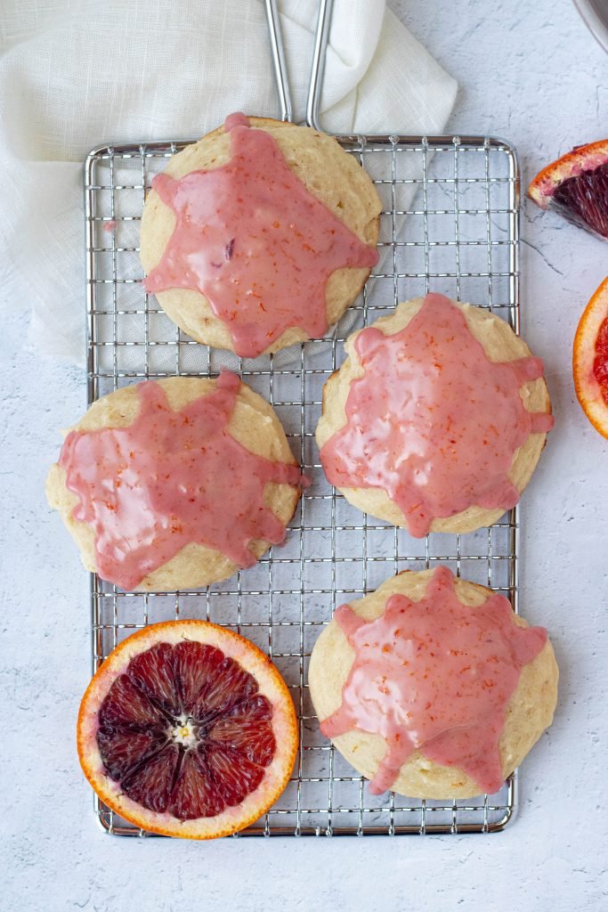 Four blood orange ricotta cookies with pink glaze. Slice of blood orange.