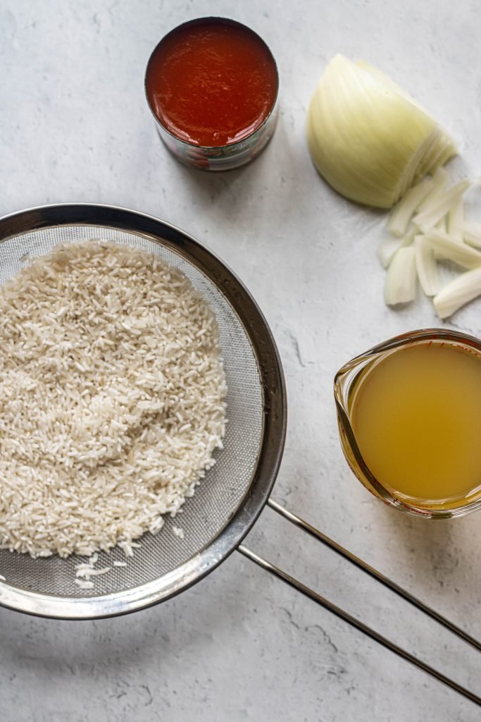 Ingredients for Mexican rice. Long grain rice in strainer, chicken broth, onion, tomato sauce
