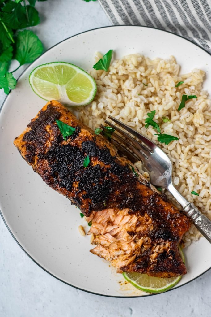 Chili Lime Salmon on white plate with side of rice and fork. Lime and Cilantro garnish