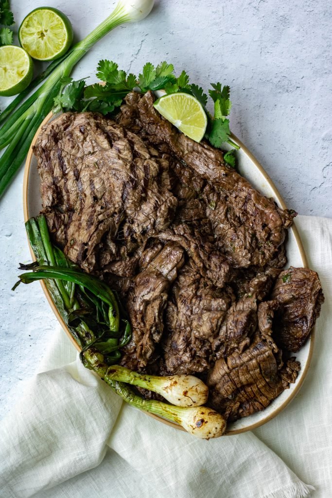 Arrachera, skirt steak, Mexican Carne Asada on platter with green onions, lime, cand cilantro garnish