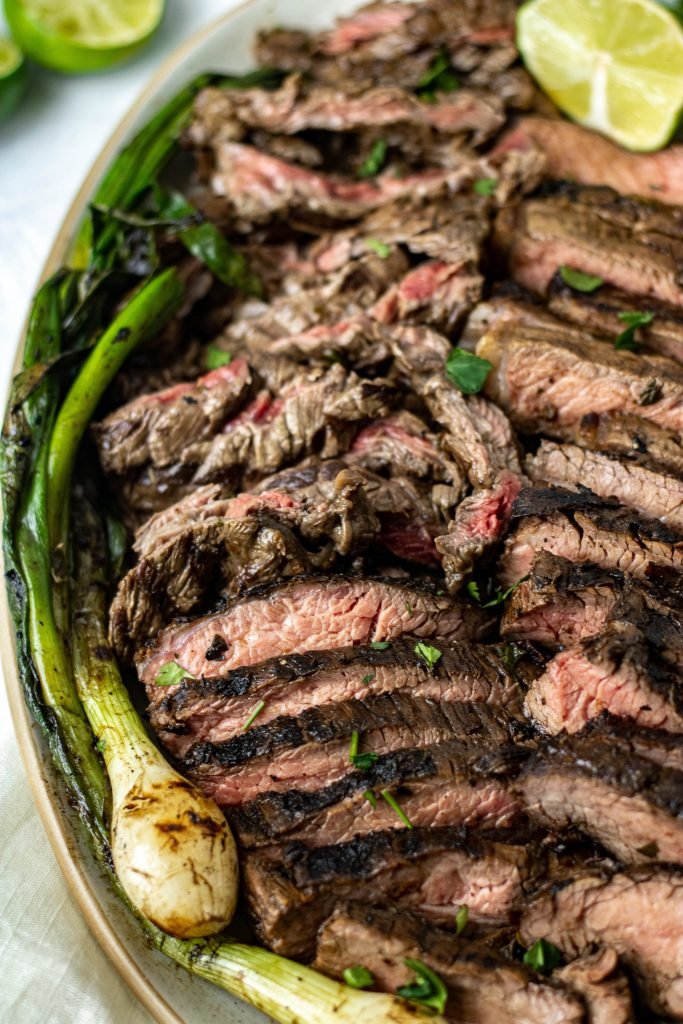 Close up of platter with sliced Mexican Carne Asada. Green onion garnish