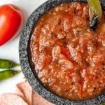 Salsa roja in stone molcajete with pepper garnish and tomato and pepper props